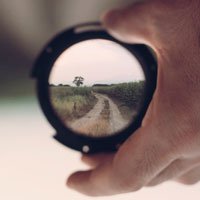 photo of hand holding magnifying glass over country road in HRExaminer article From The Vault: Questions by John Sumser published 2015-09-08