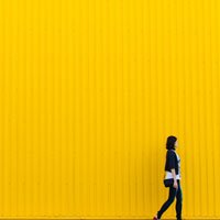 woman walking in front of bright yellow sheet metal wall on HRExaminer.com October 30, 2015 200px image
